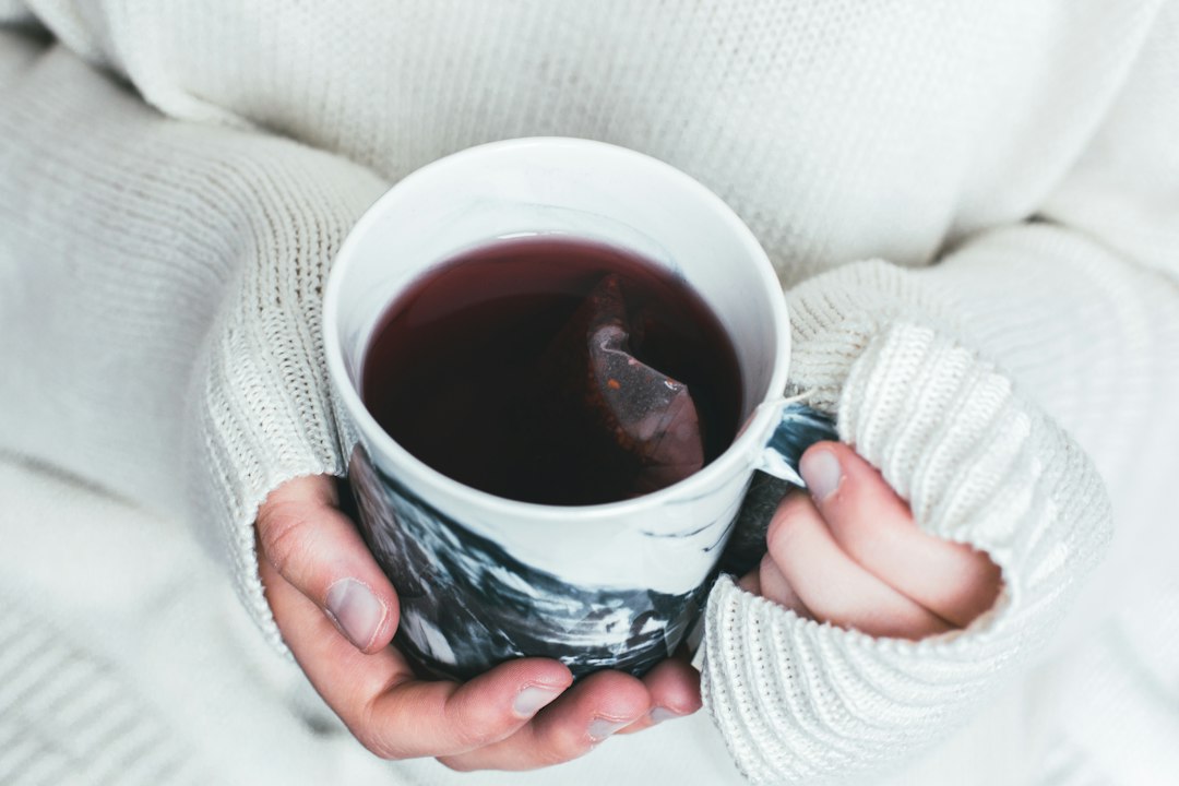 Person holding a warm cup of tea to stay comfortable in cold winter weather