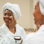 Woman with a towel on her head applying face cream from a jar