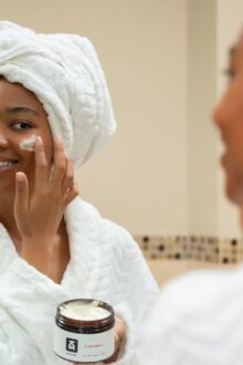 Woman with a towel on her head applying face cream from a jar
