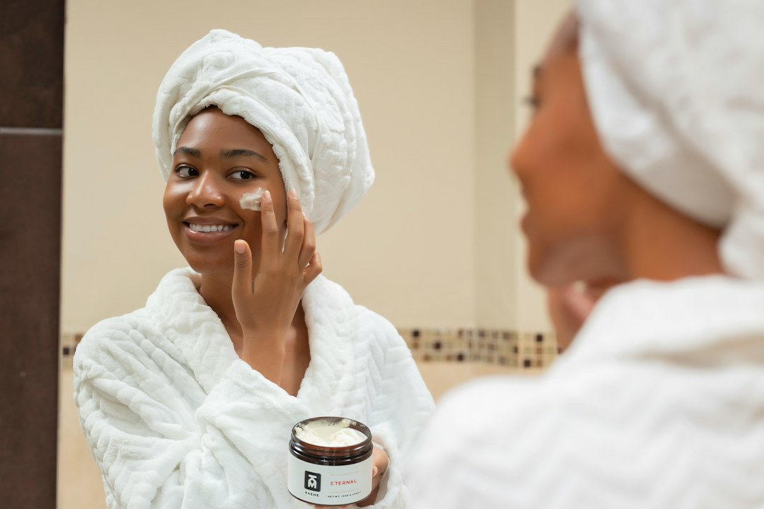 Woman with a towel on her head applying face cream from a jar